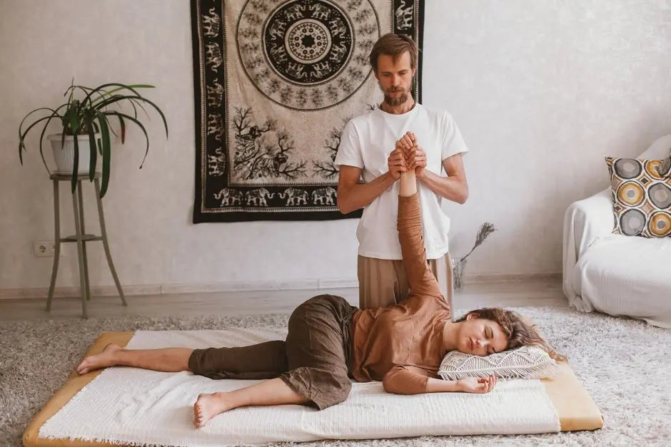 A man performs a massage on a woman lying on a carpet, both at ease in a serene indoor setting.