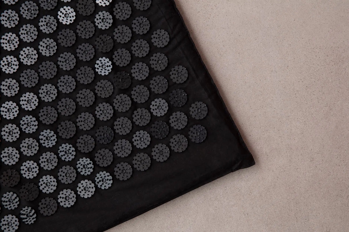 Detailed view of a black acupuncture mat on a neutral background, promoting relaxation and wellness.