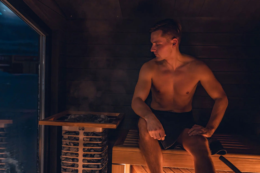 A shirtless man relaxes in a modern Nordic sauna, experiencing the warmth and benefits of steam.