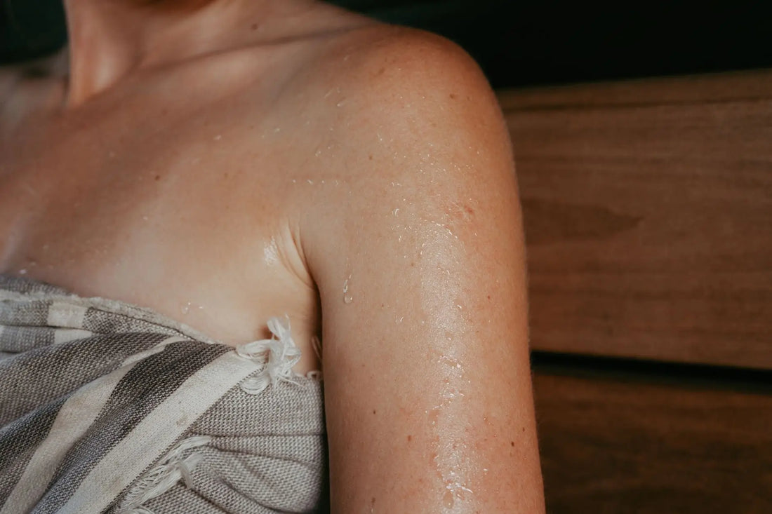 Close-up of a woman with sweat on her skin inside a sauna, highlighting relaxation and wellness.