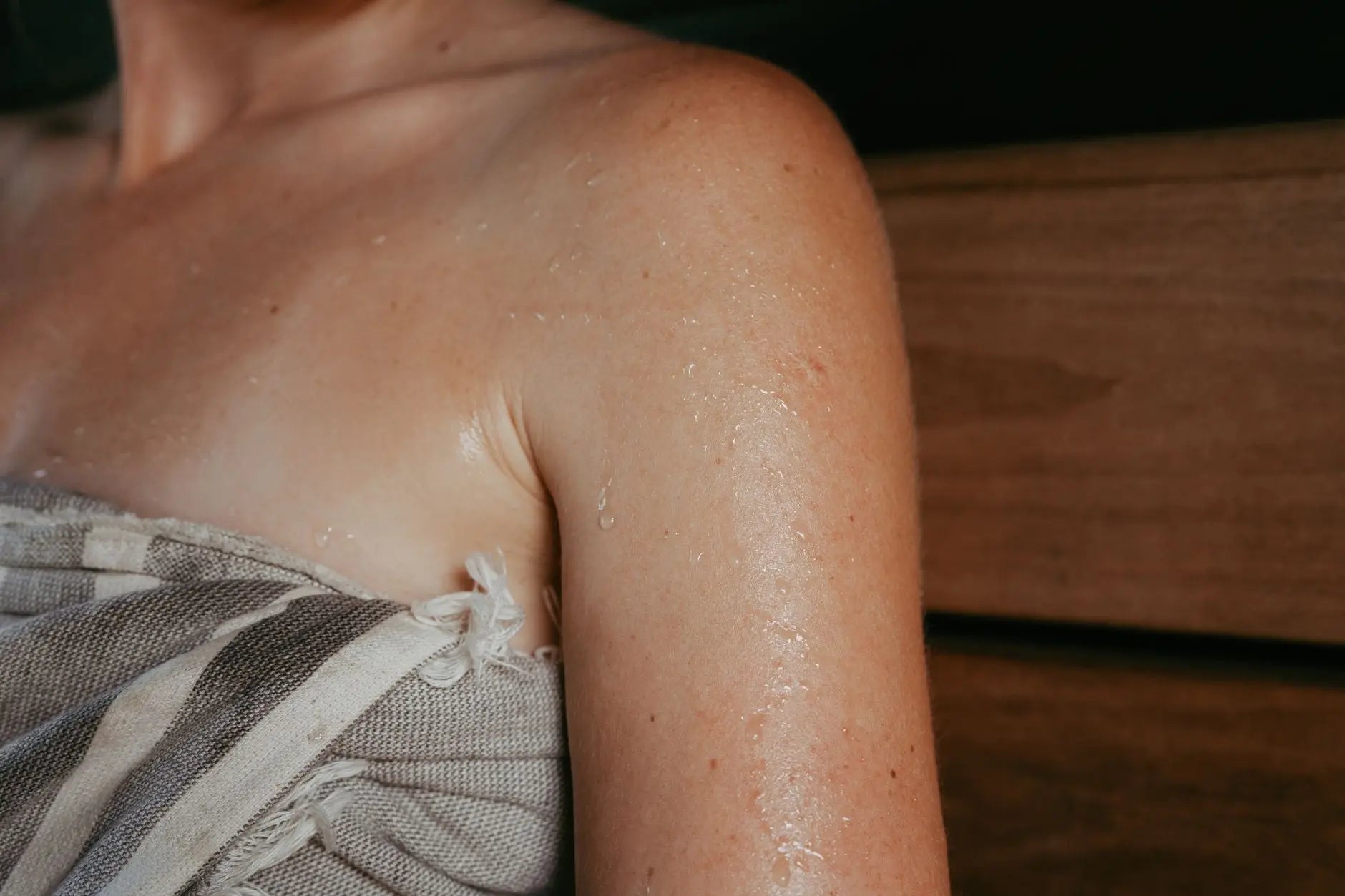 Close-up of a woman with sweat on her skin inside a sauna, highlighting relaxation and wellness.