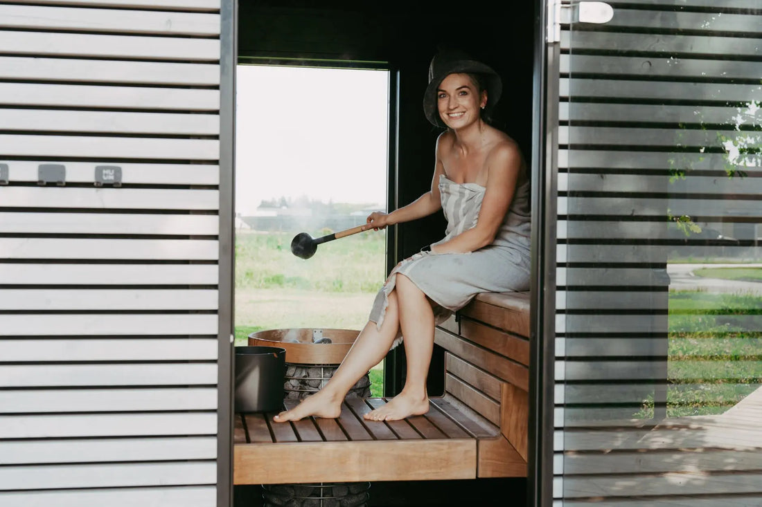 A woman in a sauna, wrapped in a towel, enjoying a relaxing steam session with a sauna hat.
