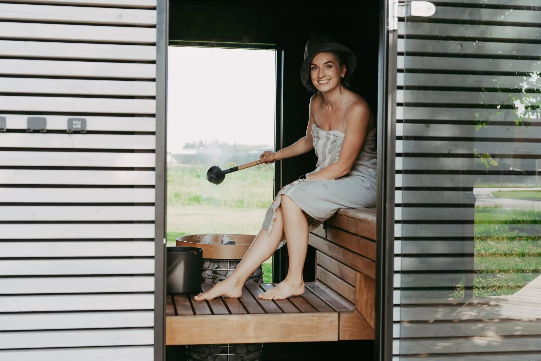 A woman in a sauna, wrapped in a towel, enjoying a relaxing steam session with a sauna hat.