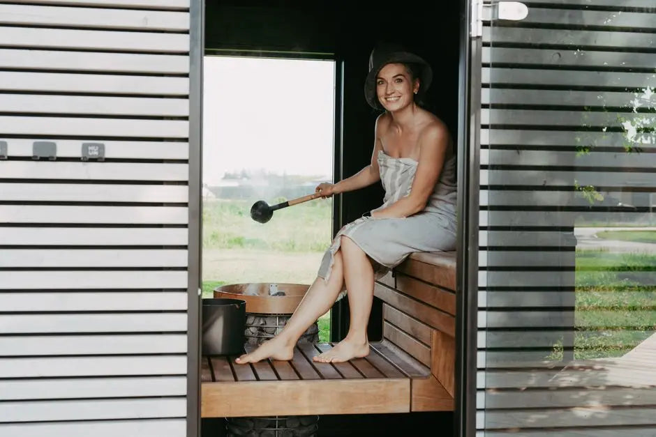 A woman in a sauna, wrapped in a towel, enjoying a relaxing steam session with a sauna hat.