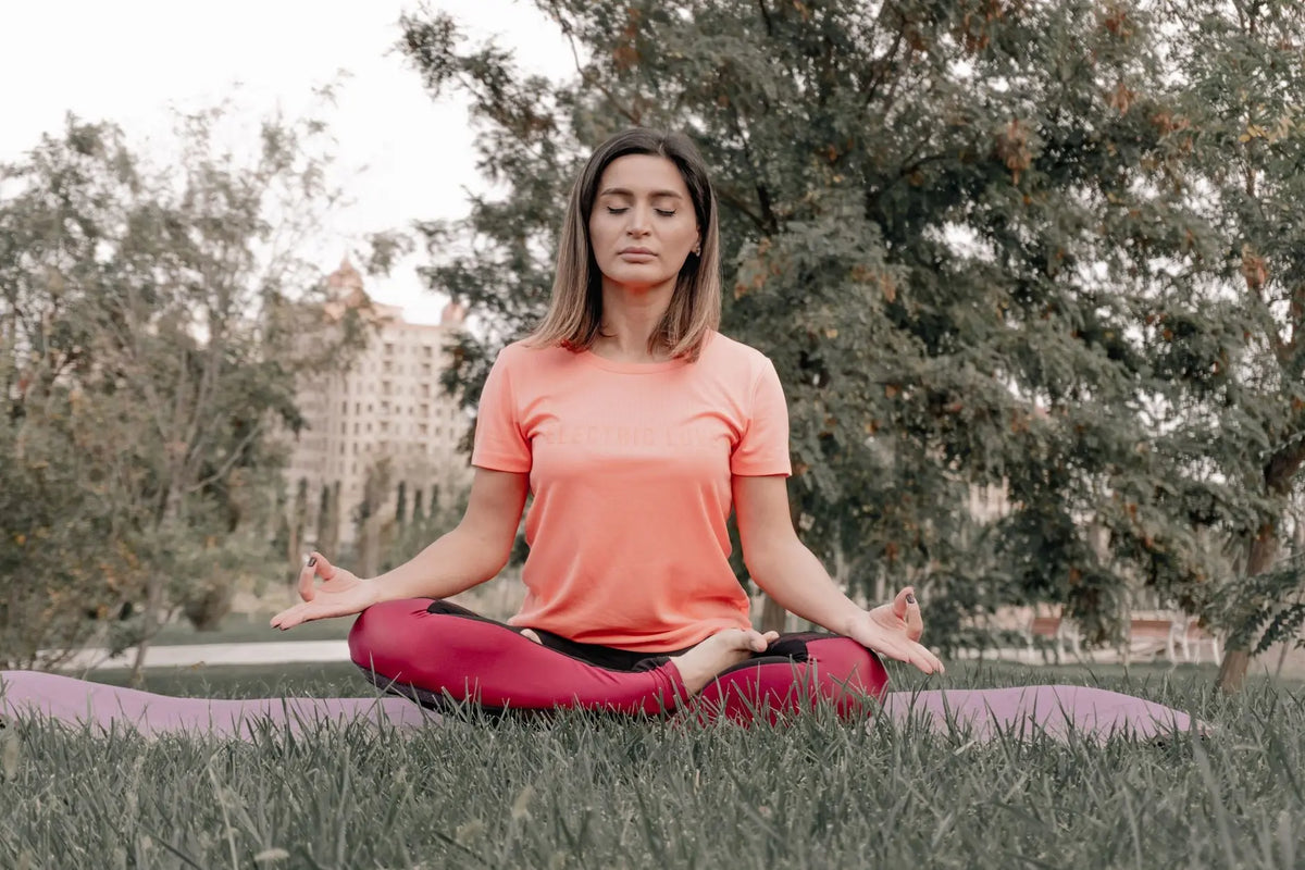 Adult woman practicing meditation on a yoga mat outdoors in a tranquil park setting.