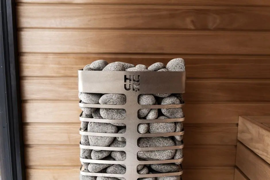 Contemporary sauna heater filled with stones, placed in a stylish wooden sauna setting.