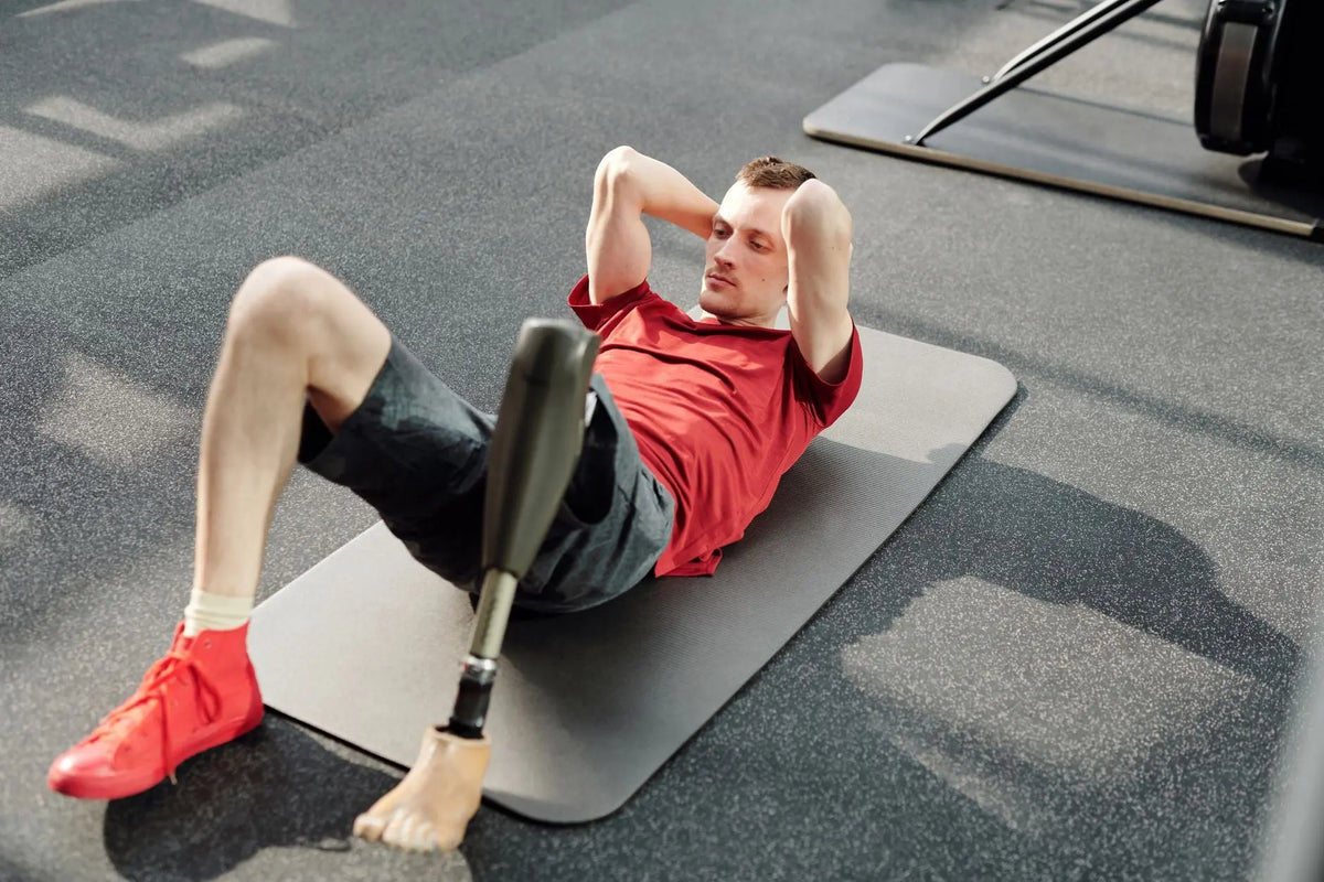 Man performing sit-ups on yoga mat using prosthetic leg in fitness gym.