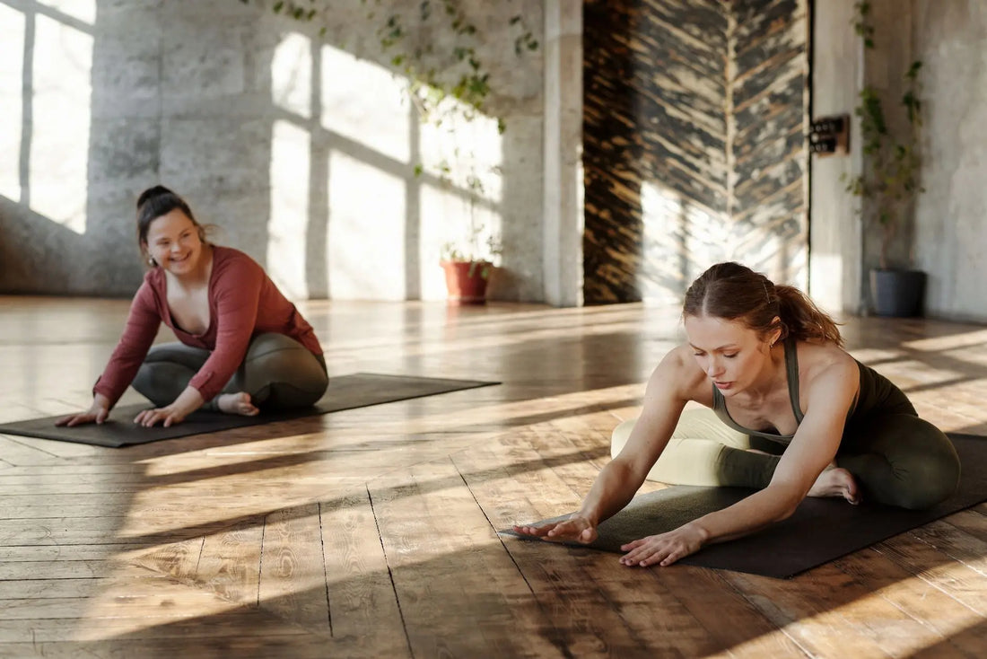 Two women practicing yoga indoors, stretching on mats in natural light.