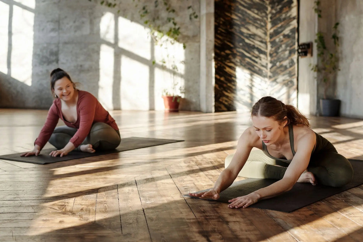 Two women practicing yoga indoors, stretching on mats in natural light.