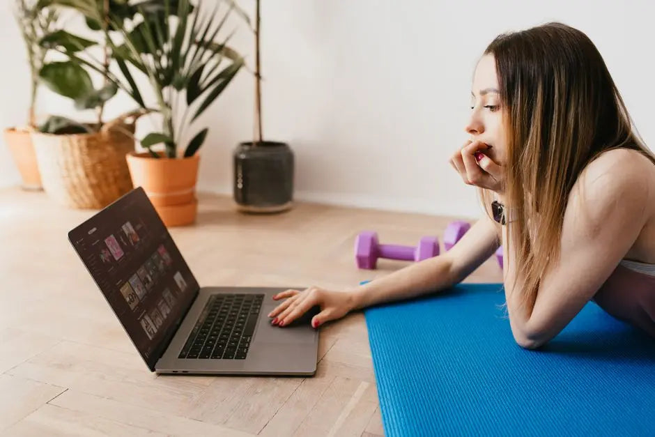 Side view of young slim female using laptop while lying on blue rubber mat during workout