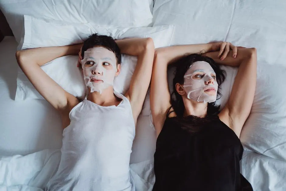 Two women enjoy a soothing relaxation with sheet masks, lying together in a comfortable setting.