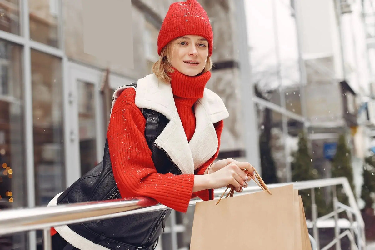 Woman in red winter clothing holding shopping bags outside in snowy weather.