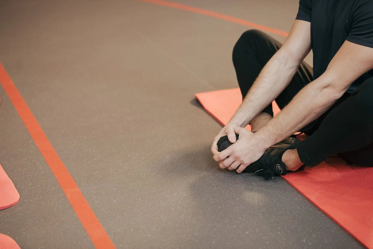Adult man stretching on a red yoga mat indoors, focusing on flexibility and fitness.