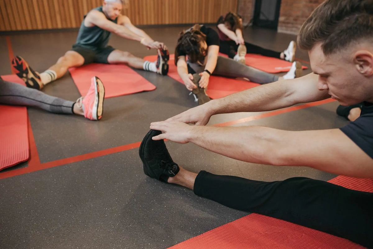 Adults participating in fitness stretching session indoors, enhancing flexibility on red yoga mats.