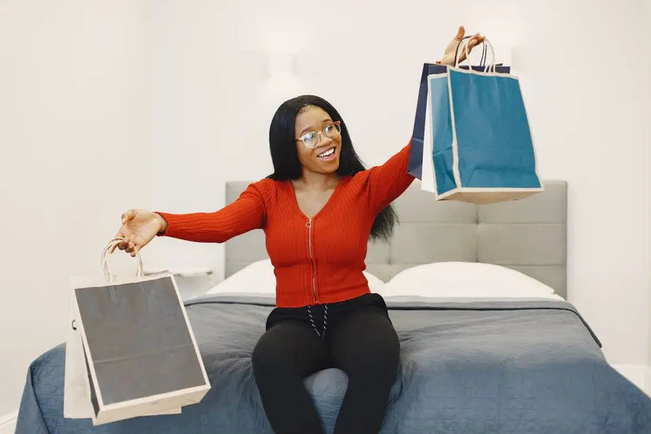 Happy woman sitting on a bed holding shopping bags, expressing excitement.