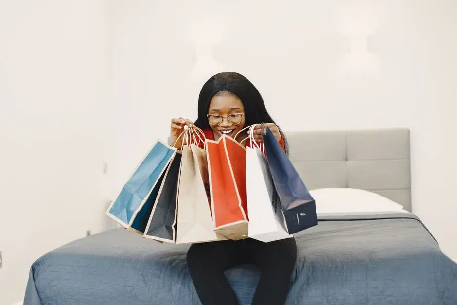 Happy woman holding colorful shopping bags, seated on a bed in a cozy bedroom.