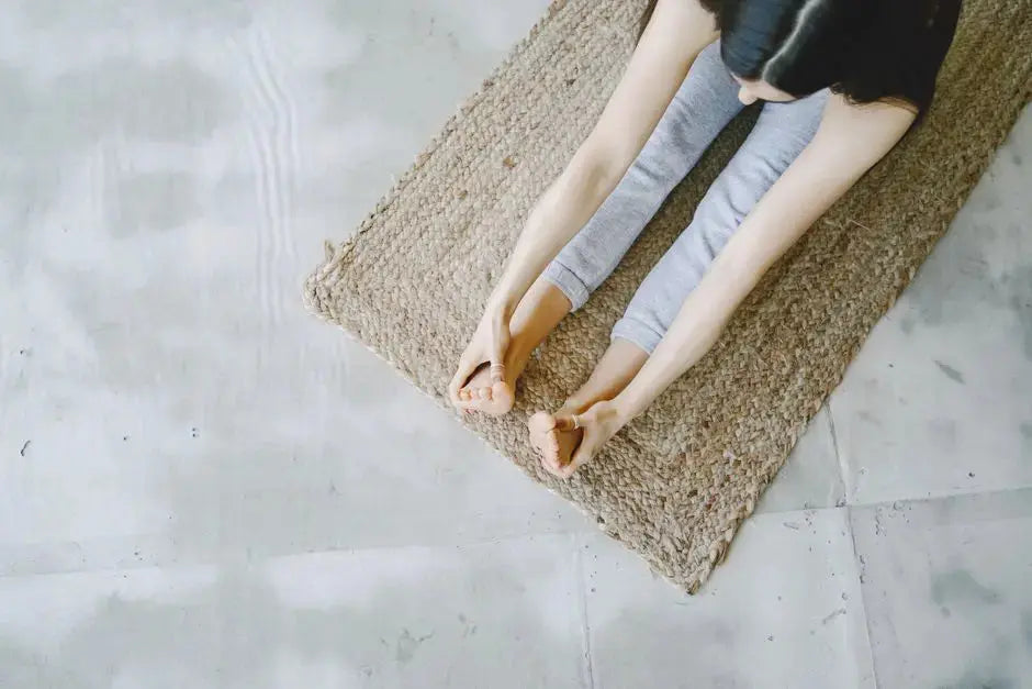 Top view of a woman practicing seated forward bend on a woven mat indoors.